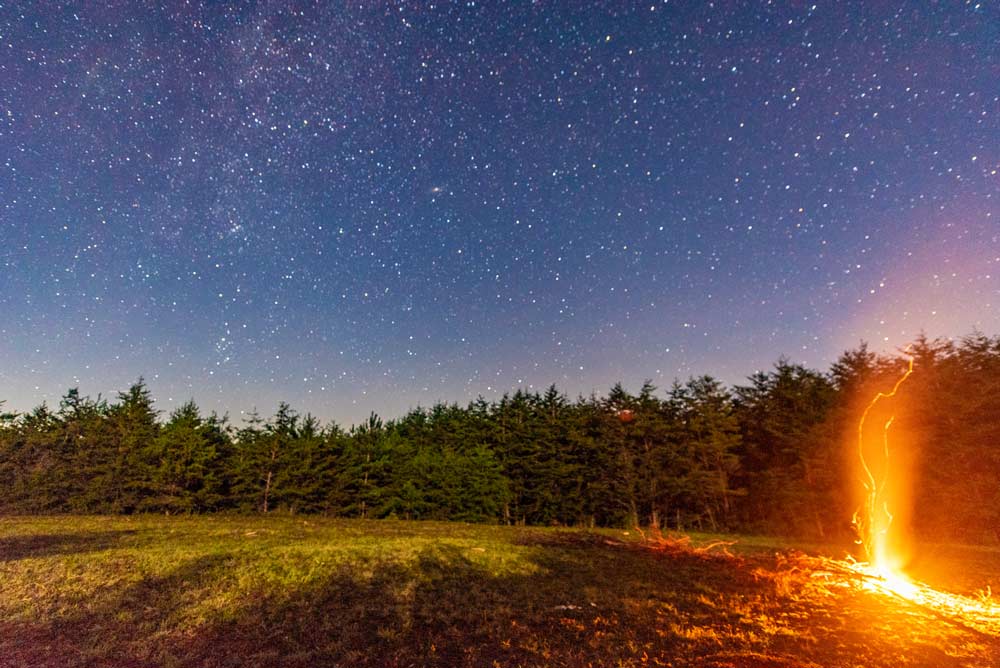 Nigh photo of the stars with a camp fire in the foreground